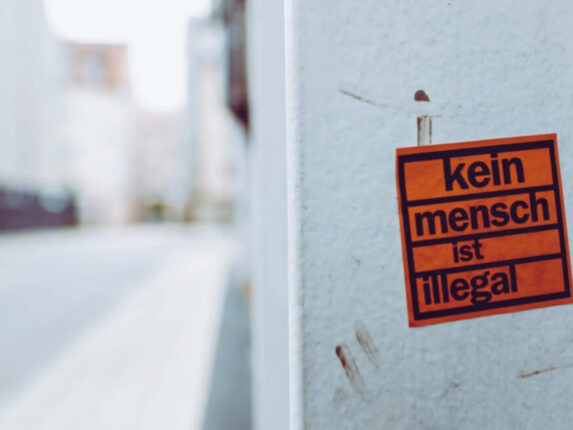 Sticker auf grauer Wand mit dem Text "Kein Mensch ist illegal!"