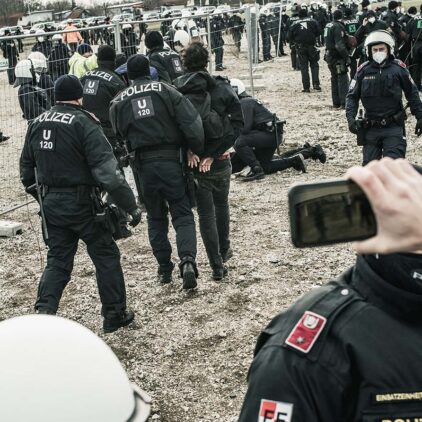Ein verwackeltes Foto von hunderten Polizist:innen, einige davon drücken Protestierende zu Boden.
