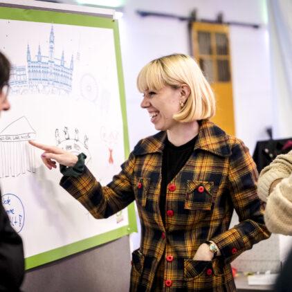 eine Frau im karierten Mantel zeigt auf eine Zeichnung auf einem Plakat bei Influence Vienna