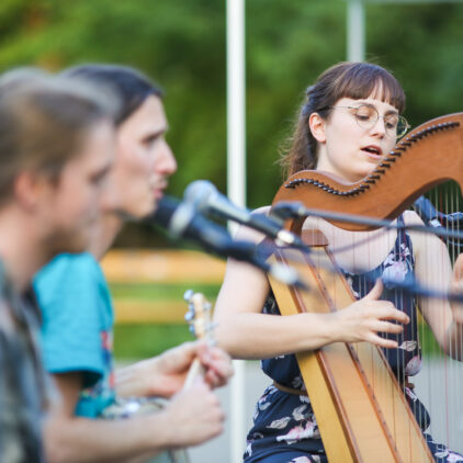 Drei Musiker:innen während eines Konzertes, im Hintergrund eine Harfe