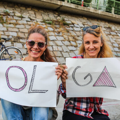 Foto von zwei Frauen, die eine Plakat in der Hand halten, mit dem text "OL" - "GA"