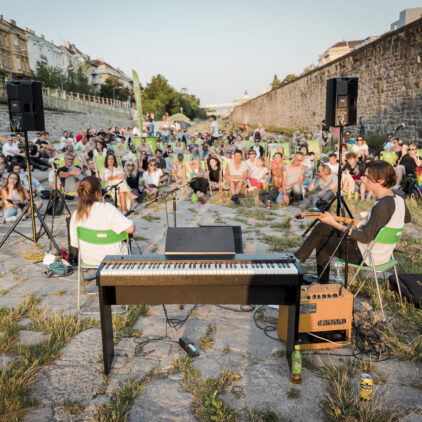 Foto einer Band, die bei Musik am Fluss auftritt, im Hintergrund sieht man das Publikum