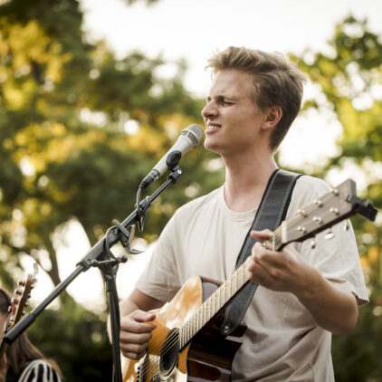 Foto eines Musikers bei einem Konzert, der singt und Gitarre spielt
