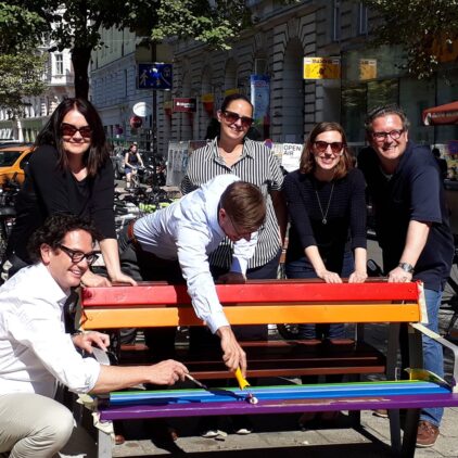 Markus Reiter und eine Gruppe von Menschen lackiert eine Parkbank in Regenbogenfarben