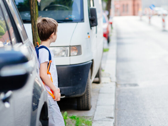 Kind steht zwischen zwei parkenden Autos und will eine Straße queren